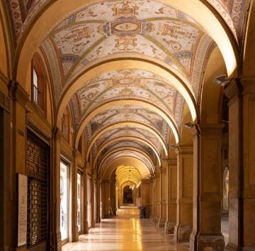 Covered portico in Bologna, Italy, with intricate ceiling frescoes and historic architectural arches